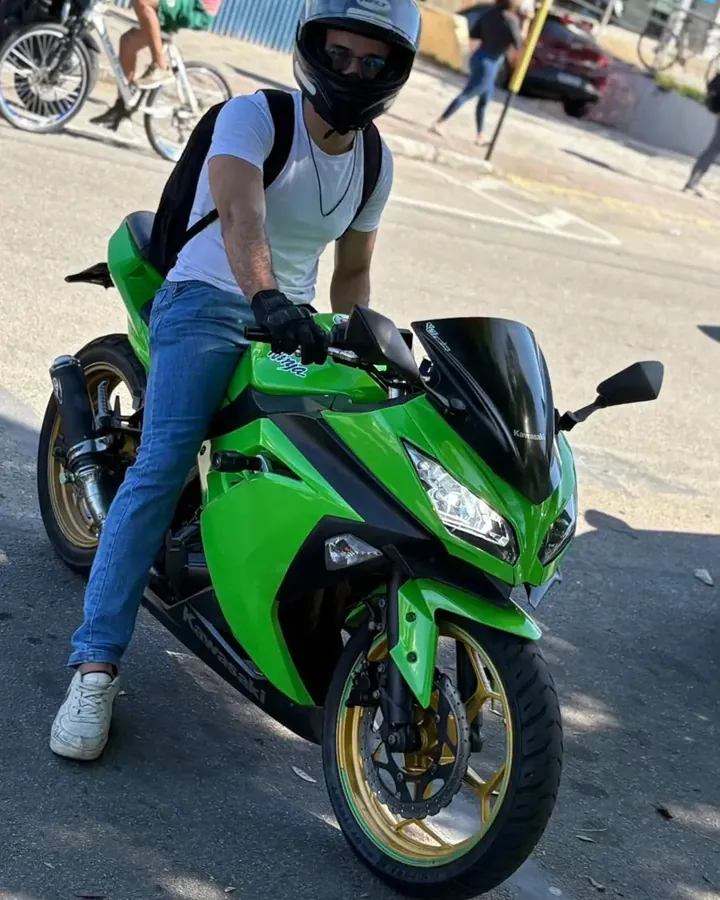 José, de capacete, sentado na Kawasaki Ninja 300 verde, parado na rua